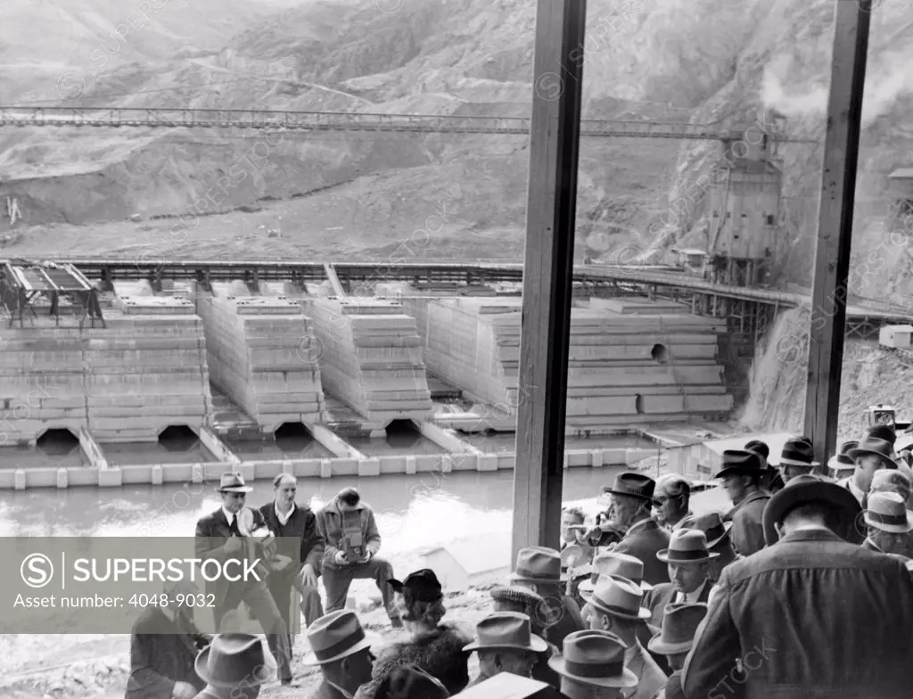 President Franklin Roosevelt inspects Grand Coulee Dam. Among many others, FDR (in lower left) listens to chief construction engineer, Frank Bucks (on right, facing group with his arm extended). FDR was touring Federal Projects in the Northwest. Oct. 2, 1937.
