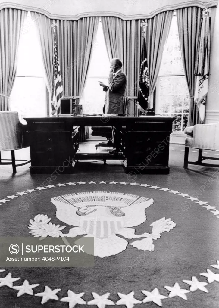 President Gerald Ford's first week in office. With Presidential seal carpet in the foreground, Ford stands during a telephone conversation in the Oval Office. Aug. 18, 1974.