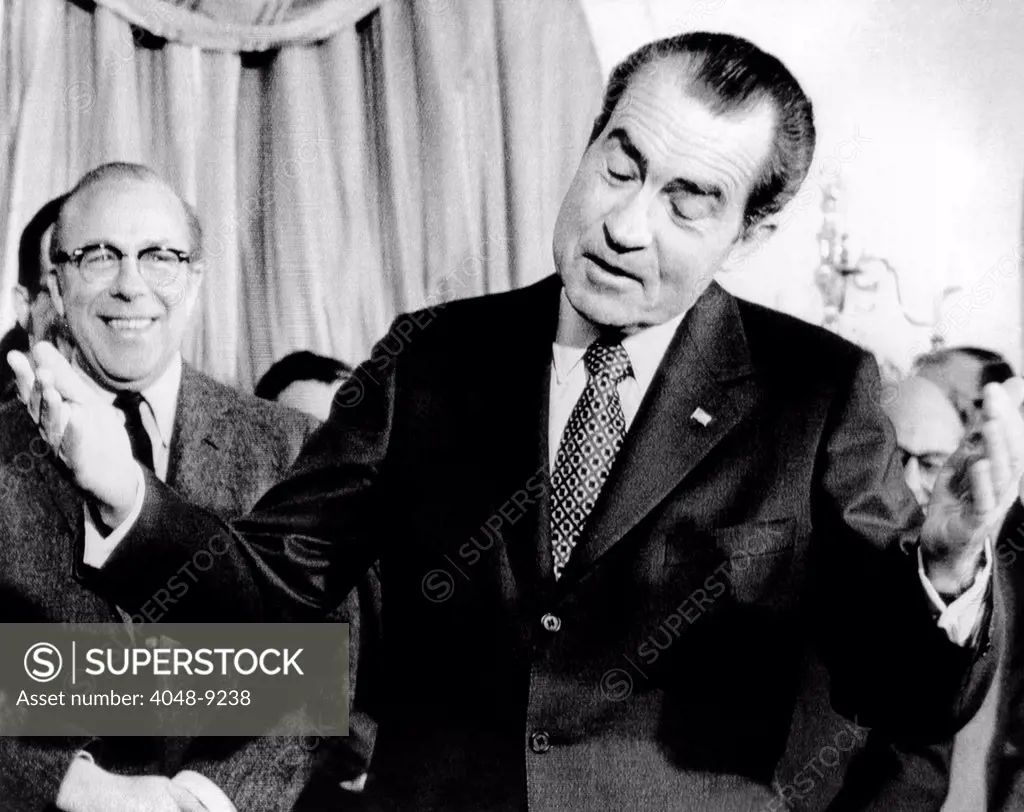 President Richard Nixon shrugs and gestures before signing the budget for fiscal 1972. The President sent to Congress a $229.2 billion budget with a built in deficit of $11.6 billion. At left is Budget Director George Shultz. June 29, 1972.