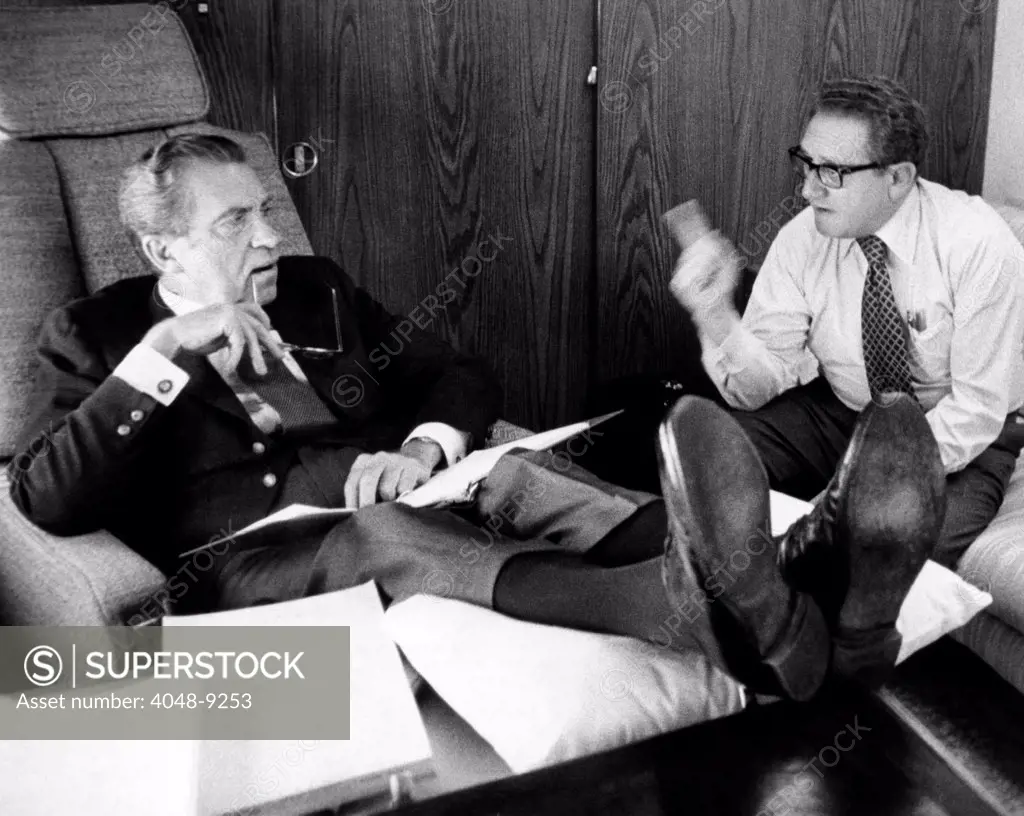 President Richard Nixon and Henry Kissinger talking on Air Force One. Nixon's multi-nation travel from June 10-19 provided little distraction from the Watergate Scandal. Nixon rests his legs on a pillow to ease an attack of phlebitis. June 26, 1974.