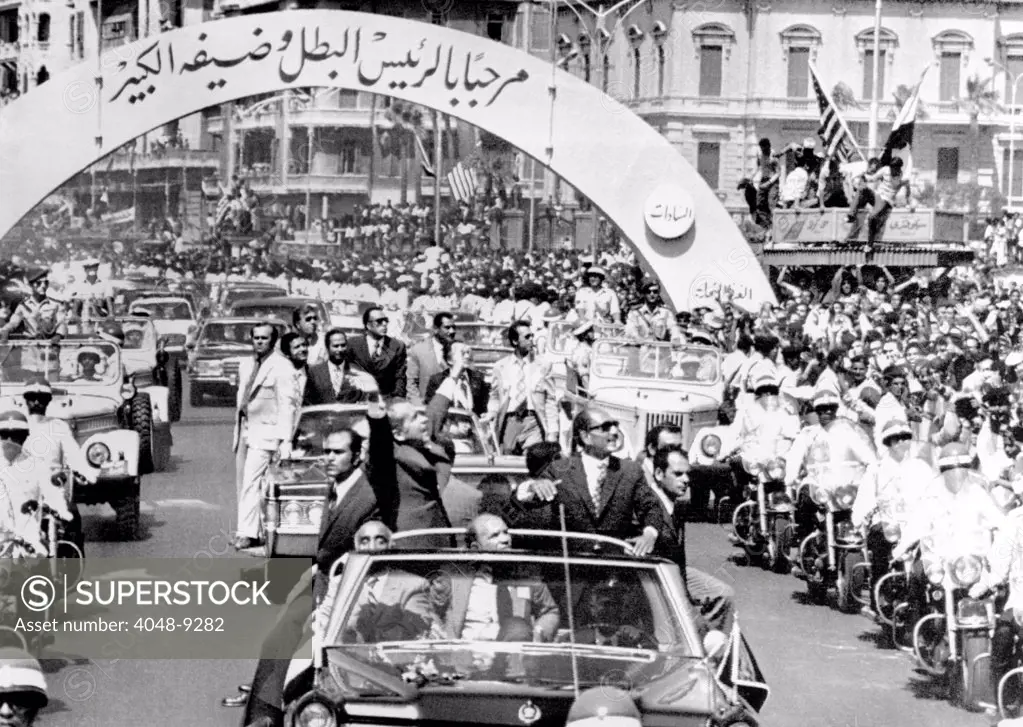 President Richard Nixon and President Sadat parade in Alexandria, Egypt. The arch reads in Arabic, 'Welcome Leader and his Great Guest.' June 13, 1974.