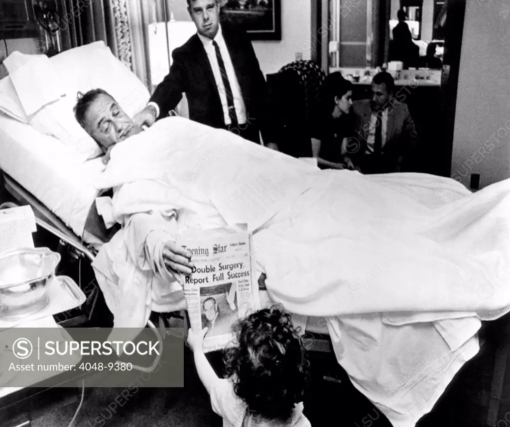 President Lyndon Johnson after gall bladder surgery. He shows a headline about his operation to Courtenay Valenti, daughter, Jack Valenti, at Bethesda Naval Hospital. In the background are Pat and Luci Nugent. Oct. XX, 1965.