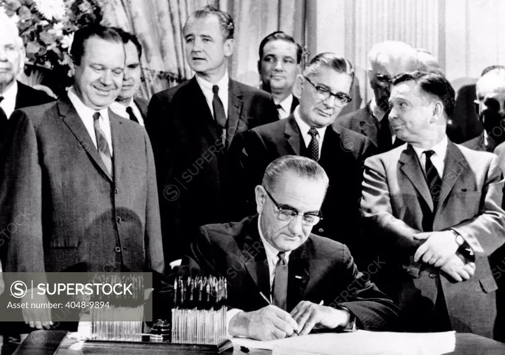President Lyndon Johnson signs a $11.5 billion tax cut bill. Standing, L-R: Russell Long, Al Ullman, George Smathers, Pat Jennings, Wilbur Mills, John McCormack, Carl Albert. Feb. 26, 1964.