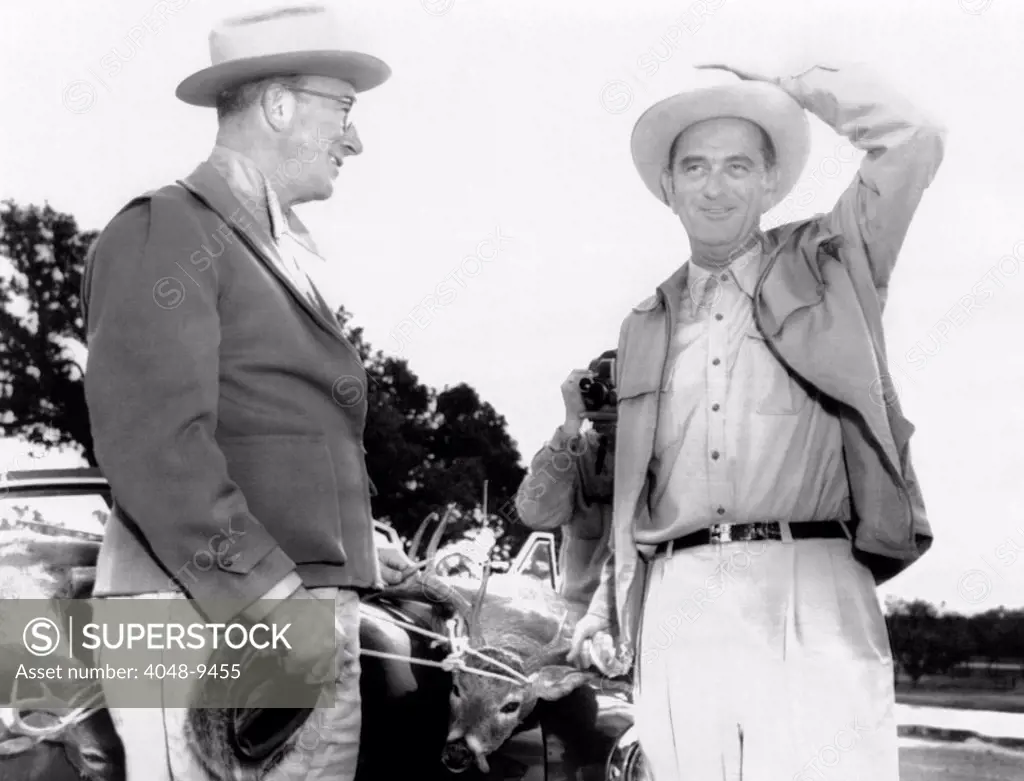 President Lyndon Johnson entertains Senator Estes Kefauver at the LBJ Ranch. There are two dead deer tied to the car behind them, trophies from their hunt. Nov. 23, 1955.