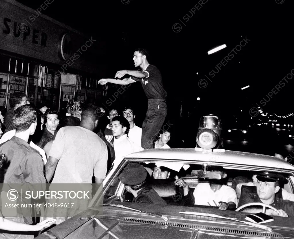Puerto Rican youth standing on a police car, urges the crowd to go home and aid in dispersing neighborhood groups. Spanish Harlem, New York City, July 23, 1967.