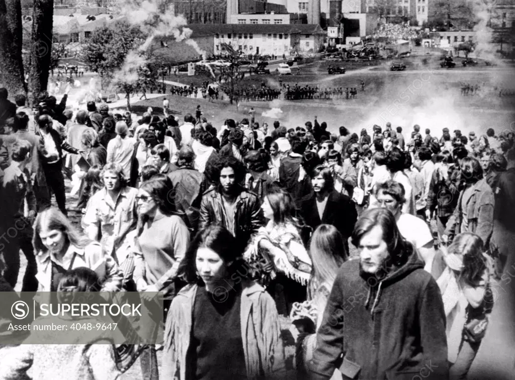 Kent State University students disperse as National Guardsmen (in background) fire tear gas and then bullets into crowd of 500 on the commons. The gutted out building on the upper right is the ROTC building which was destroyed by fire 2 days earlier. May 4, 1970.
