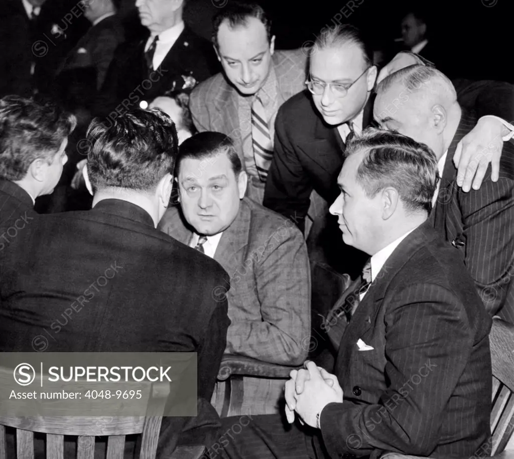 George 'Bugs' Moran on trial for forgery. Moran (center) and Frank Parker (right) talk with defense attorney George Bieber (back to camera) in court in Chicago. Moran and Parker are on trial for conspiracy to forge and counterfeit $62,000 worth of American Express money orders. Standing behind are Attorneys Arnold Harris (left) and Howard Levy. Jan 3, 1939.