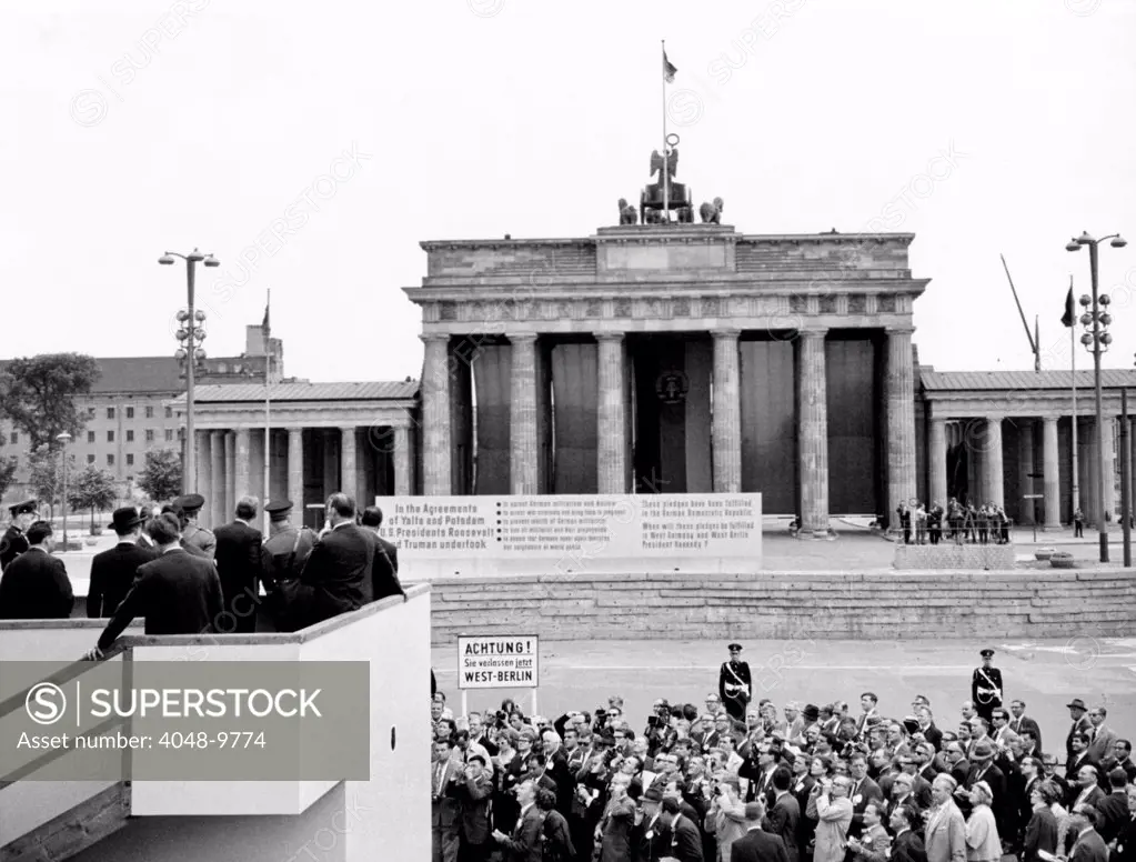 President John Kennedy visits the Berlin Wall. From a specially-built platform at the Brandenburg Gate, President Kennedy looks over the Communist wall dividing East and West Berlin. East German police erected a sign saying that Nazis and militarists have been banned in East Germany but not in the West. June 26, 1963.