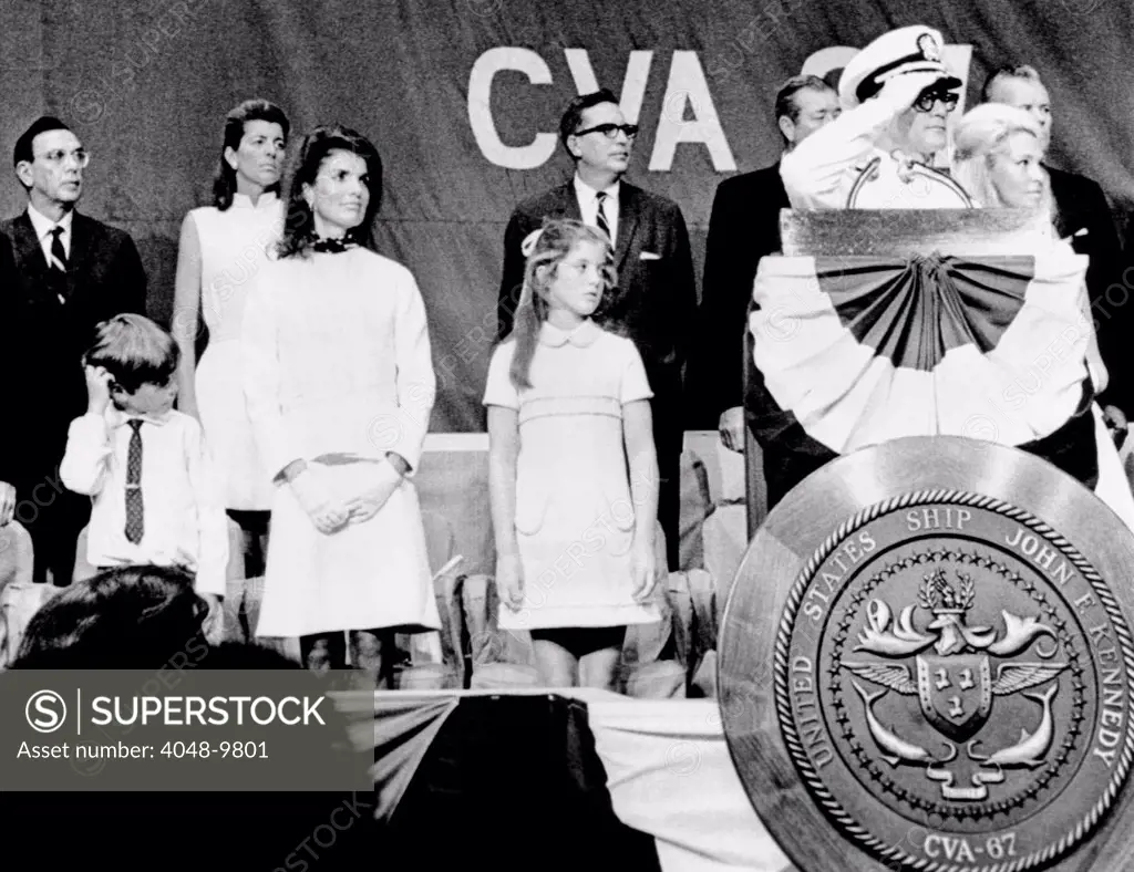 Captain Earl Yates (on right, saluting), the commanding officer of the new aircraft carrier USS John F. Kennedy during the commissioning ceremonies. Kennedy's widow Jacqueline and children, Caroline and John Jr. look on. Also Attending were Patricia Kennedy Lawford (back row) and Joan Kennedy (far right). August 7, 1968.
