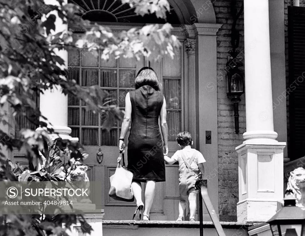 Jacqueline Kennedy and her son, 3 year old John F, Kennedy Jr. entering their Georgetown Federal era home. The house was staked out by photographers, tourists, and even tour buses. After less than a year in the residence, Mrs. Kennedy moved to New York City. May 24, 1964.