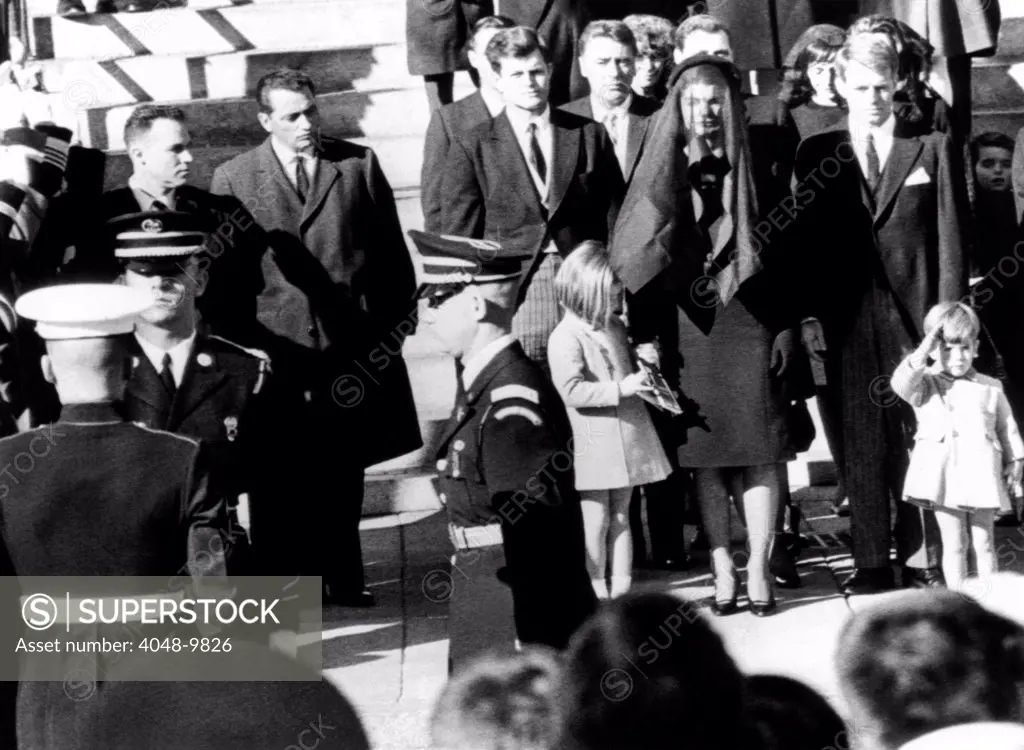 Three year old John F. Kennedy Jr. salutes his father's flag draped coffin after funeral mass at St. Matthew's Cathedral. Family members from center, L_R: Sen. Edward Kennedy, Caroline Kennedy, Peter Lawford, Jacqueline Kennedy, Robert Kennedy, and John Jr. Nov. 25, 1963.