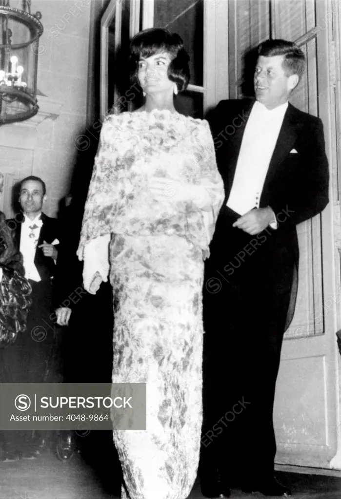 President and Jaqueline Kennedy in Paris. The First Lady wears and white and pink straw lace evening dress during their visit to Paris. They are leaving the French Foreign Ministry for a reception at Elysee Palace. May 31, 1961.