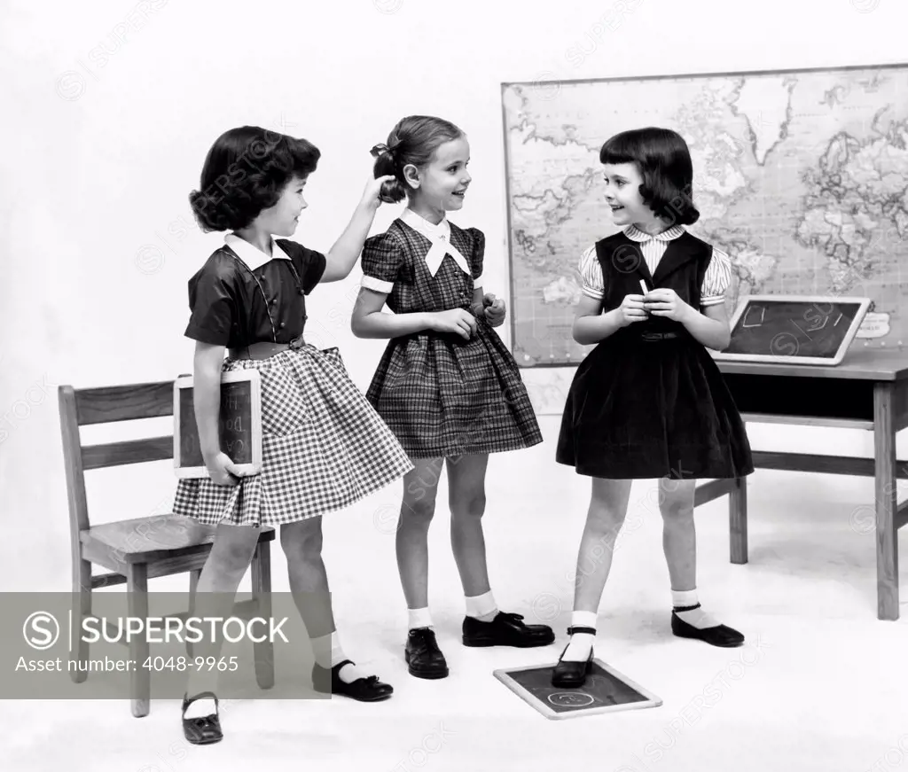 Little girls school dressed in 1953. They echo the 'Dior's New Look' with their full gathered skirts and belted waists, worn with crisp white ankle socks.