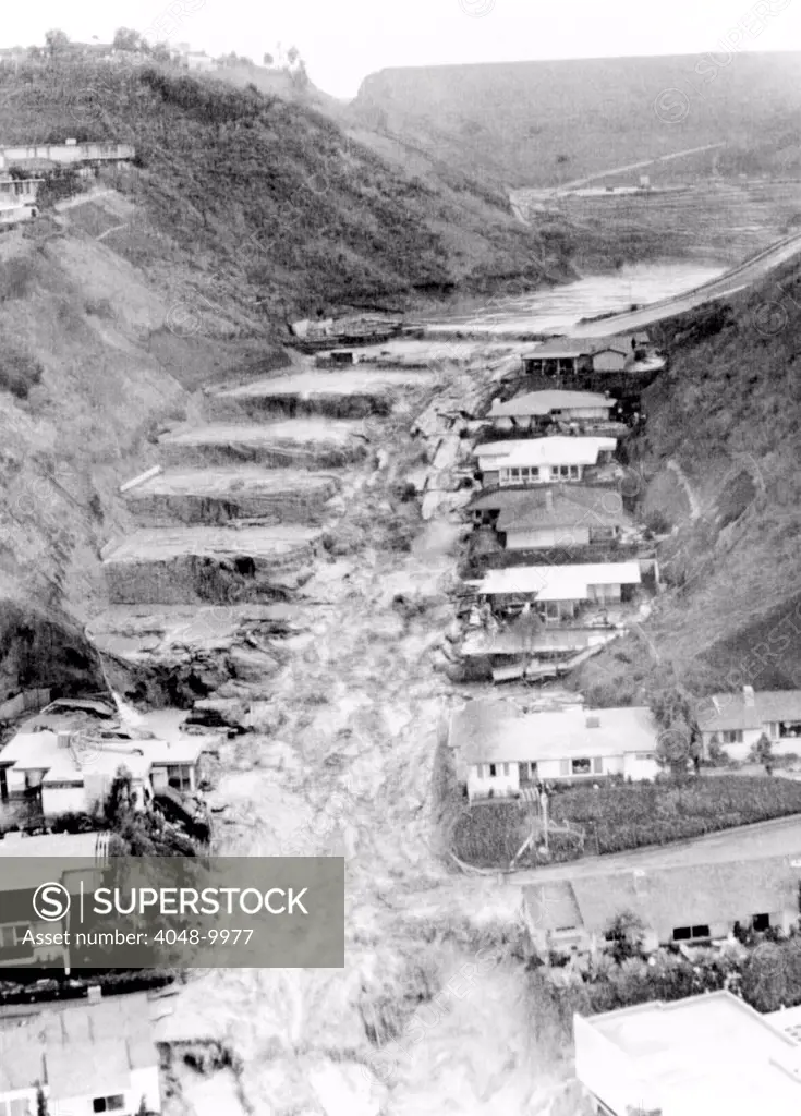 Tons of water cascade from the Baldwin Hills Reservoir. At right, homes remain intact but at left, only step-like plateaus remain. 277 homes were destroyed and 5 people were killed. Dec. 14, 1963.