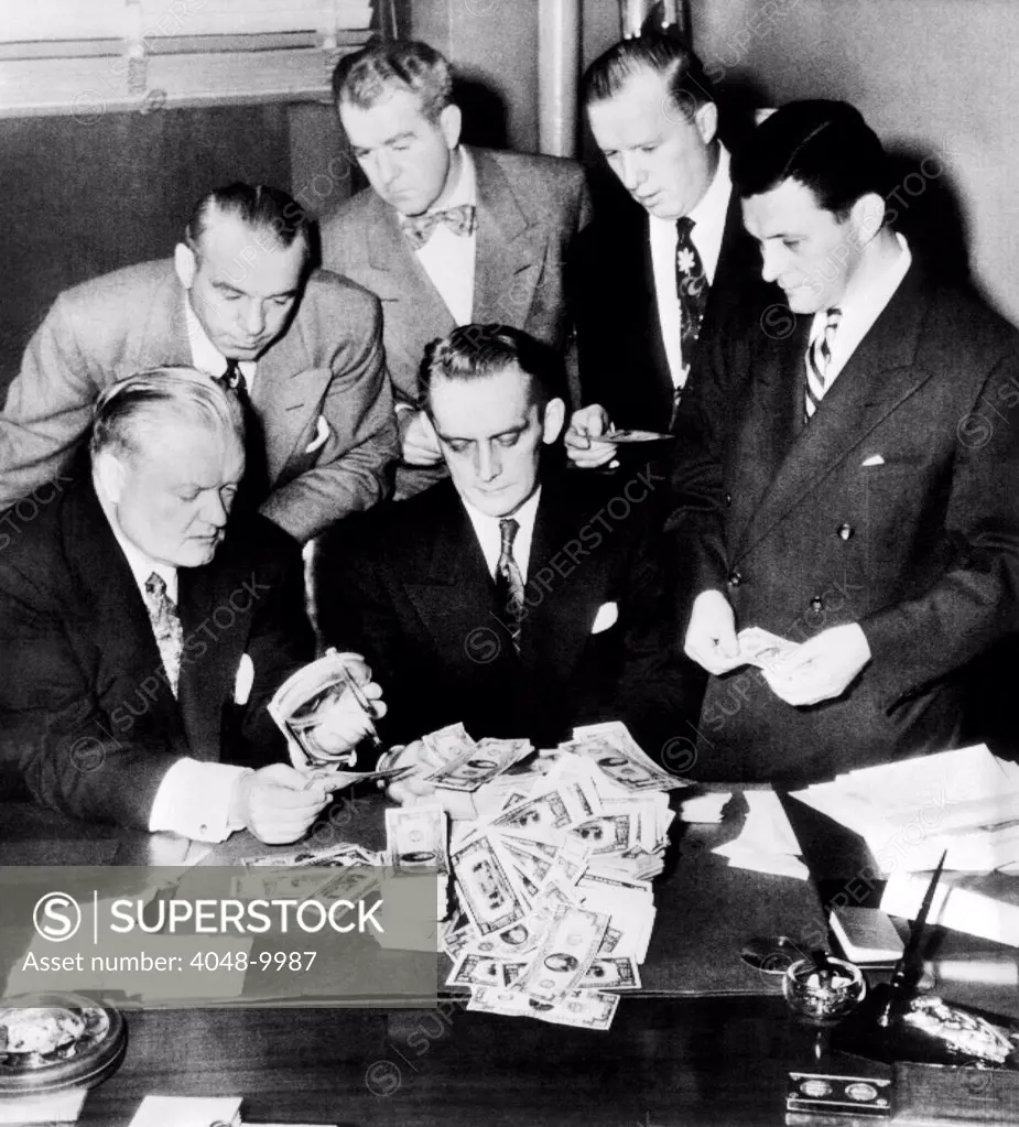 Federal and State men looking at part of $100,000 of counterfeit money seized in Chicago, Feb, 2, 1952. Seated (L- R): John Boyle, States Atty, Harry Anheier, Chief of Secret Service, Standing, Lt. James Oakey, States Atty., Investigator, Everett J. Ryan, U.S. Asst. Atty., Tom Mclnerney, States Investigator, and Otto Kerner Jr., U.S. Dist. Atty.