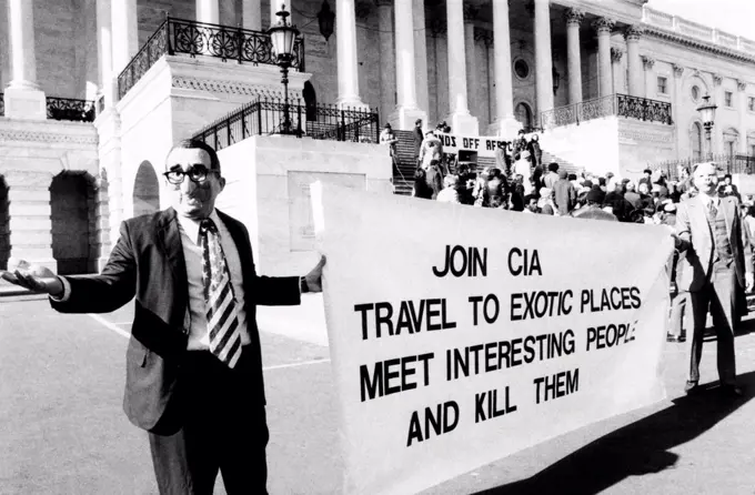 Rally protesting U.S. involvement in Angola. Demonstrators in front of the Capitol wear masks of Henry Kissinger and a pig. Their sign reads, 'Join CIA. Travel to exotic places, Meet Interesting People and Kill Them'. Jan. 22, 1976.
