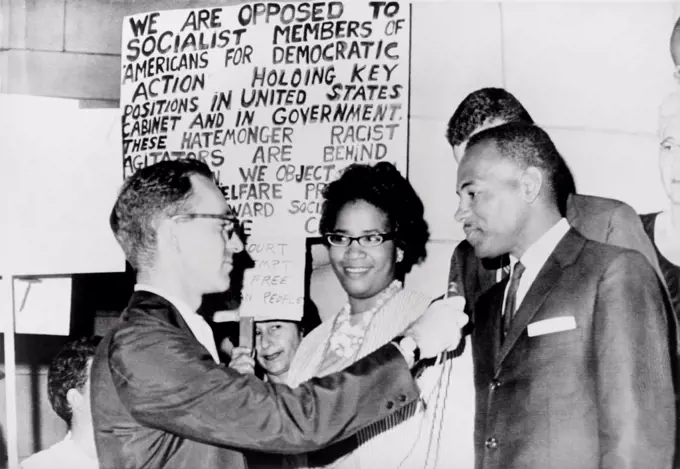 James Meredith and wife in front of segregationist poster as they talk to a reporter. The Fifth U.S. Circuit Court of Appeals ordered his admission to the University of Mississippi. Sept. 25, 1962.