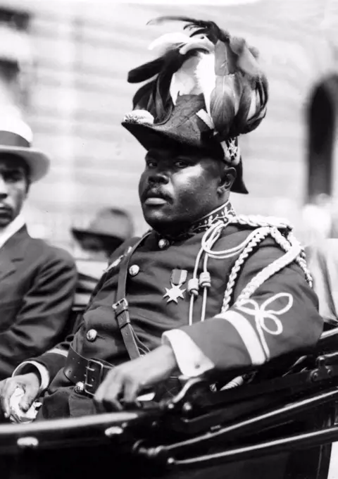 Marcus Garvey, the Negro Moses, rides through the streets of Harlem, New York City, amid delegates resplendent in plummage and golden braid.  August 1922.