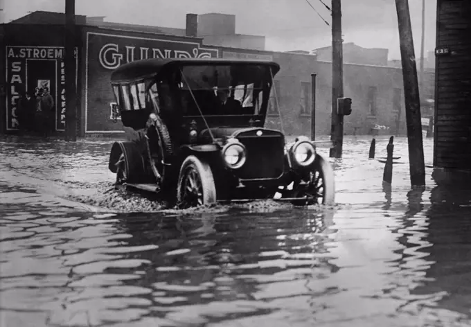 An automobile drives through axel high water on a flooded Cleveland street, probably in 1913. The early cars were built with high clearances to navigate the rough roads of the time. The Great Flood of 1913 was Ohio's largest weather disaster of the early 20th century (BSLOC_2017_17_95)