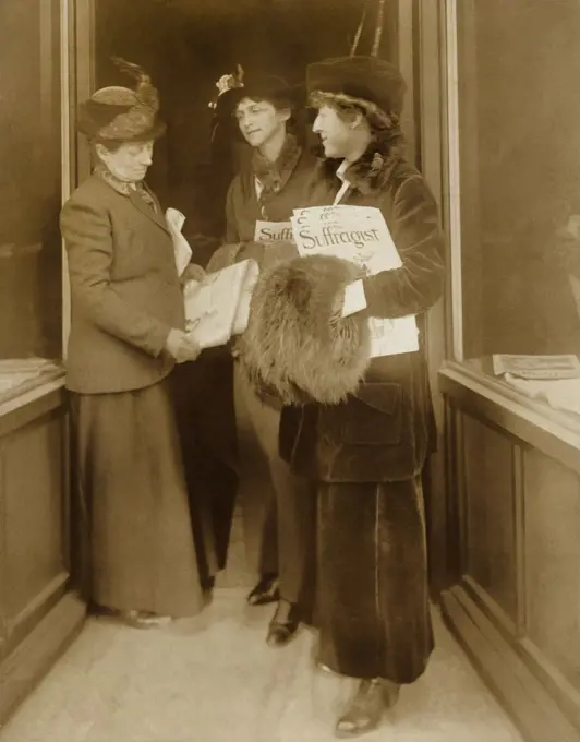Jeanette Rankin, with hat, fur muff, and several issues of THE SUFFRAGIST, the magazine of the militant National Women's Party with two women, who also hold copies of the paper. Rankin was later serve two terms in Congress representing Montana.