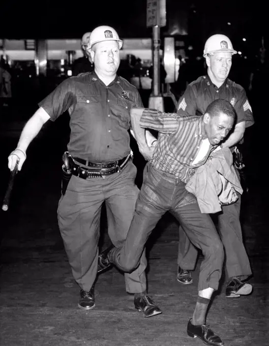 An African American who police accused of wielding a knife is taken into police custody. It was the fourth night of rioting on Harlem's 125th Street, July 21, 1964.