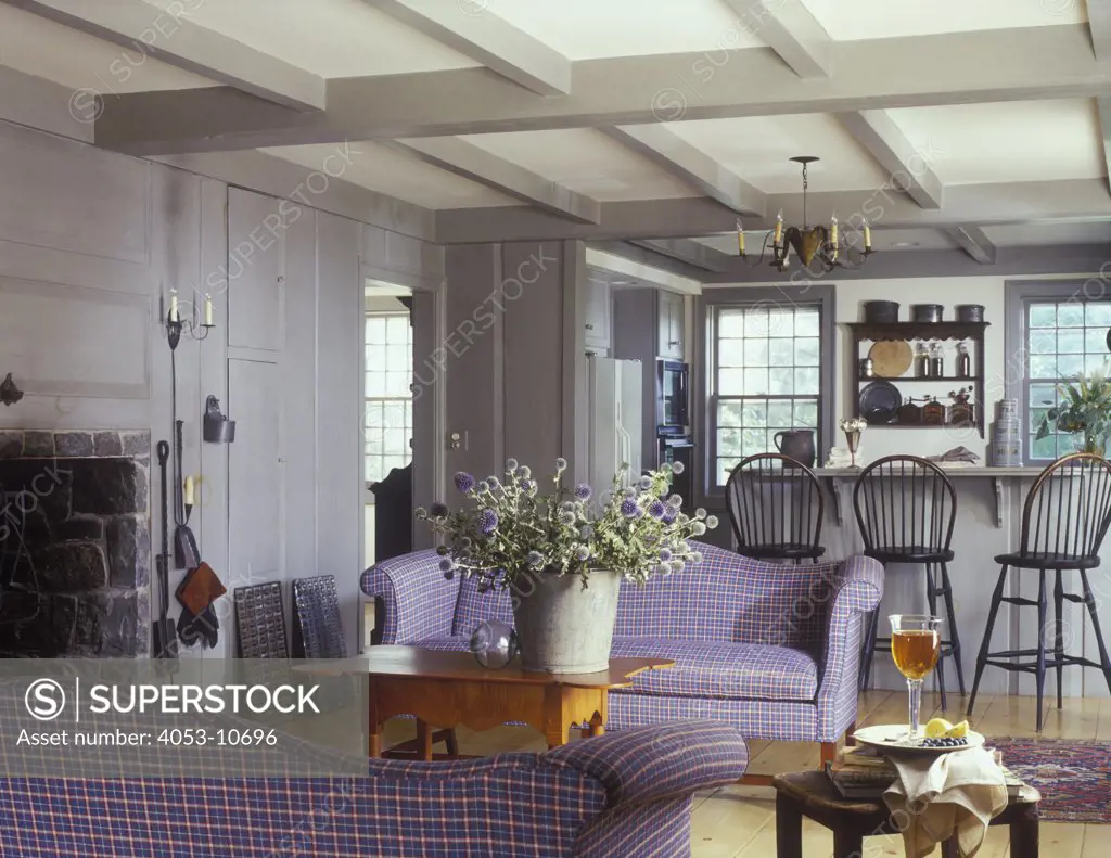 LIVING ROOMS - Clean Country Living style, exposed beams, gray wood paneling, plaid sofas, kitchen in background, counter with Windsor back bar chairs, tin bucket filled with globe thistles, beamed ceiling, camel back sofas, period country with a clean contemporary feel