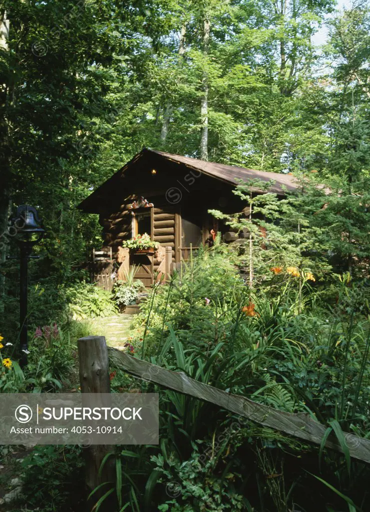 EXTERIORS: log cabin in the woods, wild overgrown, wooded area, fence, bell at stepping stone path