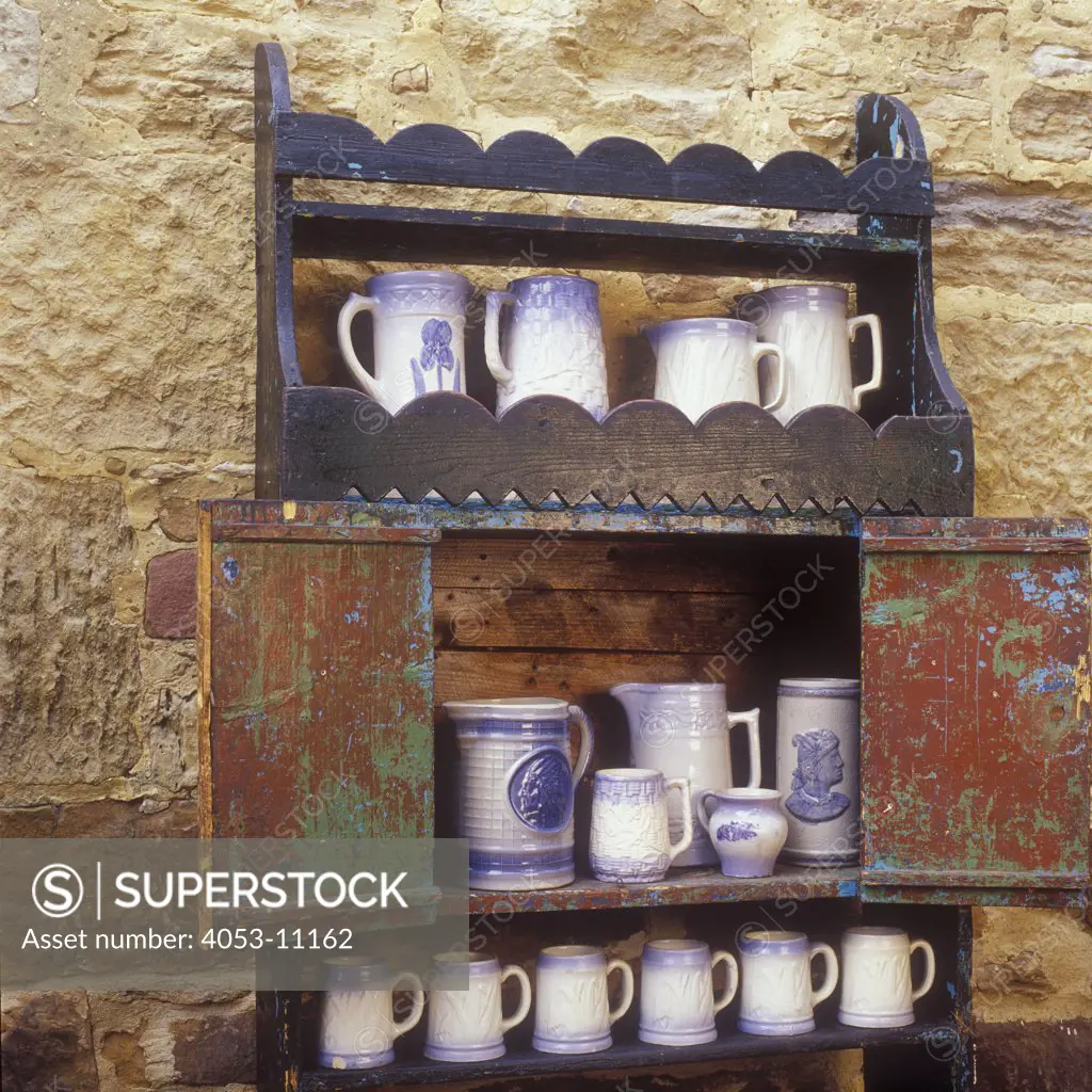 COLLECTIONS DISPLAYS - An antique open cupboard made by German immigrant in 1850. A collection of Salt Glaze Pottery on shelves, stone wall as background, Mineral Point Wisconsin, Jail House Antiques