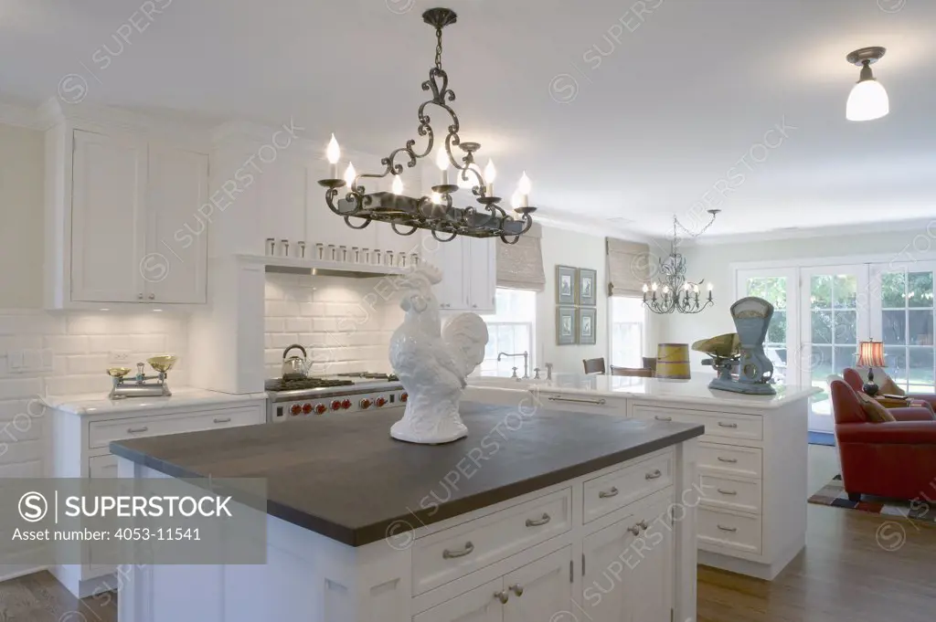 KITCHENS: Overall view of contemporary traditional  style kitchen and family great room, dark wood countertop on island white ceramic rooster, iron chandelier, blue counter scale, marble counters, large painted brick wall, white cabinets, sitting area beyond with red leather chairs,