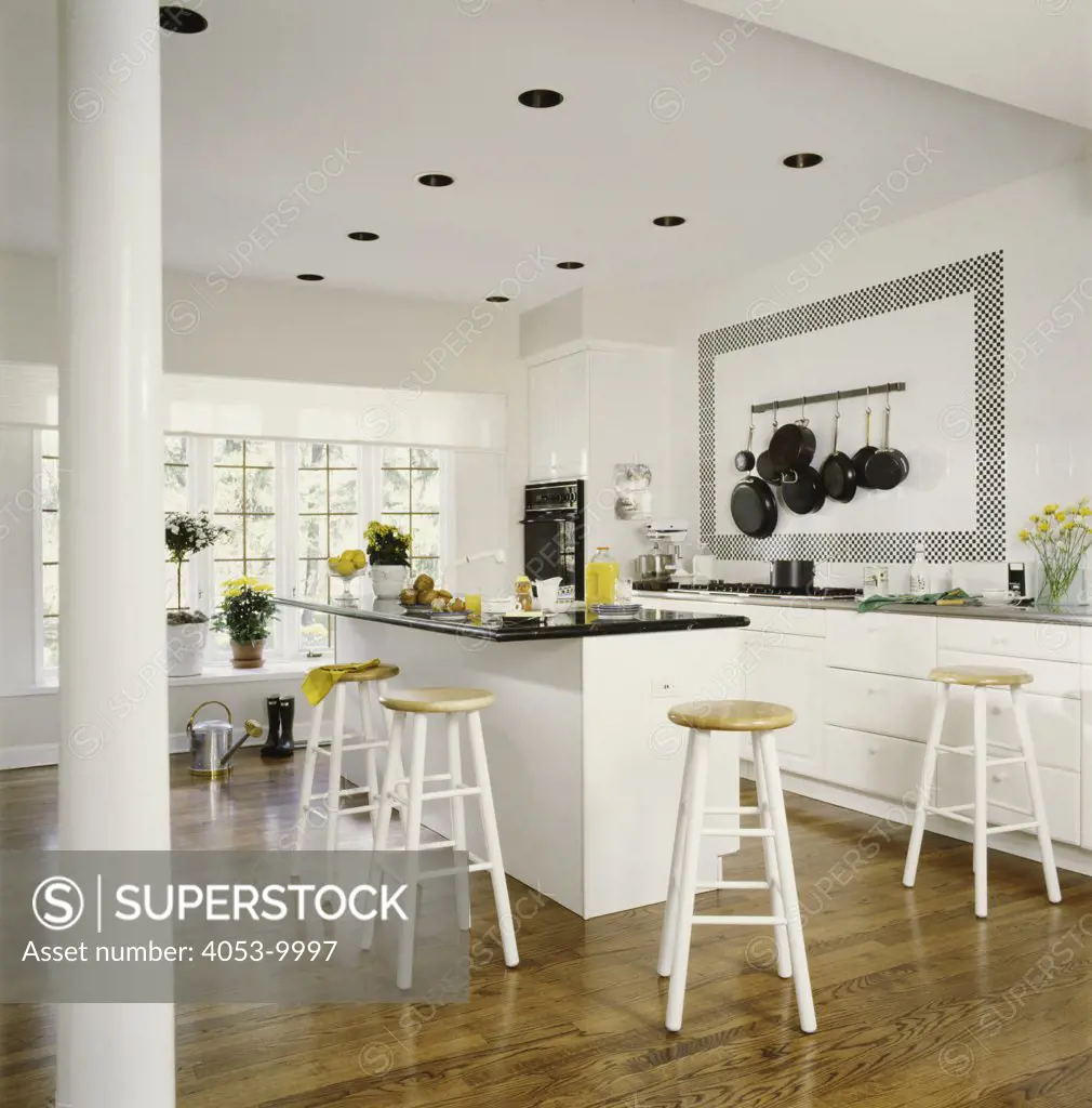 KITCHEN: White kitchen with breakfast bar and stools, black and white tiles, and wooden floor, yellow accents, pot rack on wall