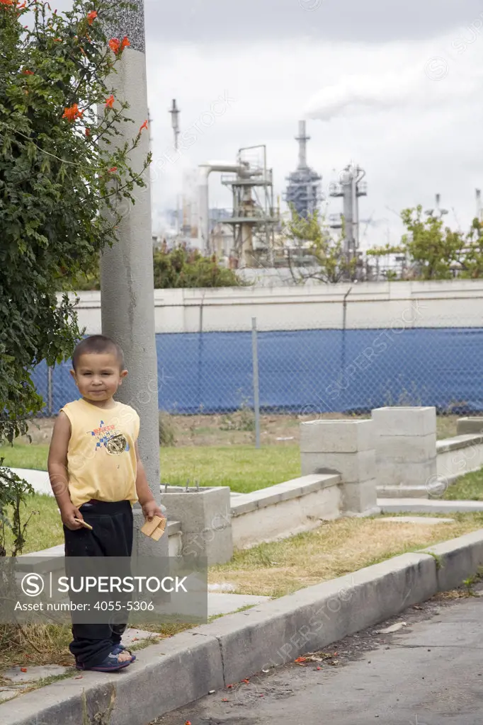 Young latino boy plays in the shadow of an oil refinery. Wilmington has one the highest risks of cancer due to it's proximity to the Port of Los Angeles at Long Beach, and the several oil refineries in the vicinity. CBE (Communities for a Better Environement) Toxic Tour takes attendees through various toxic sites in and around Los Angeles, Wilmington, Los Angeles, California, USA