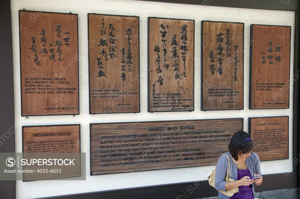Girl sitting in front of wodden tablets of Haiku and Tanka poems. Japanese Village Plaza, Little Tokyo, Los Angeles, California, USA