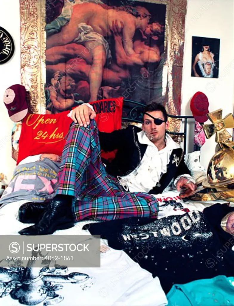 A Portrait of a man; Laying on his bed surrounded by Vivienne Westwood T shirts and Clothing; UK 2002