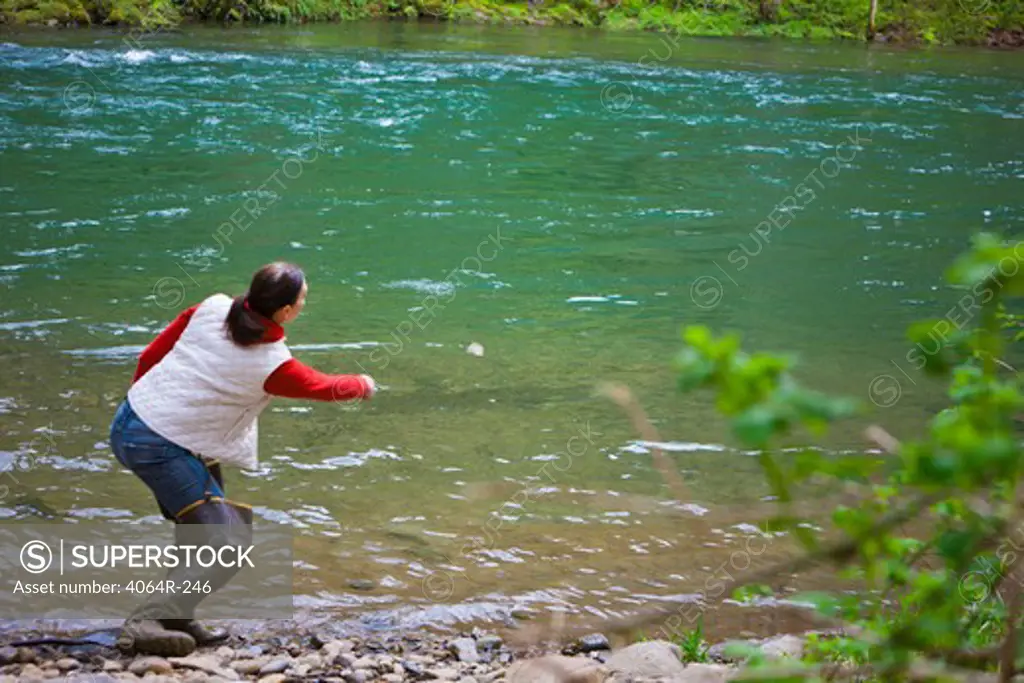 USA, Washington, Vancouver, Rear view of woman skipping stones on river
