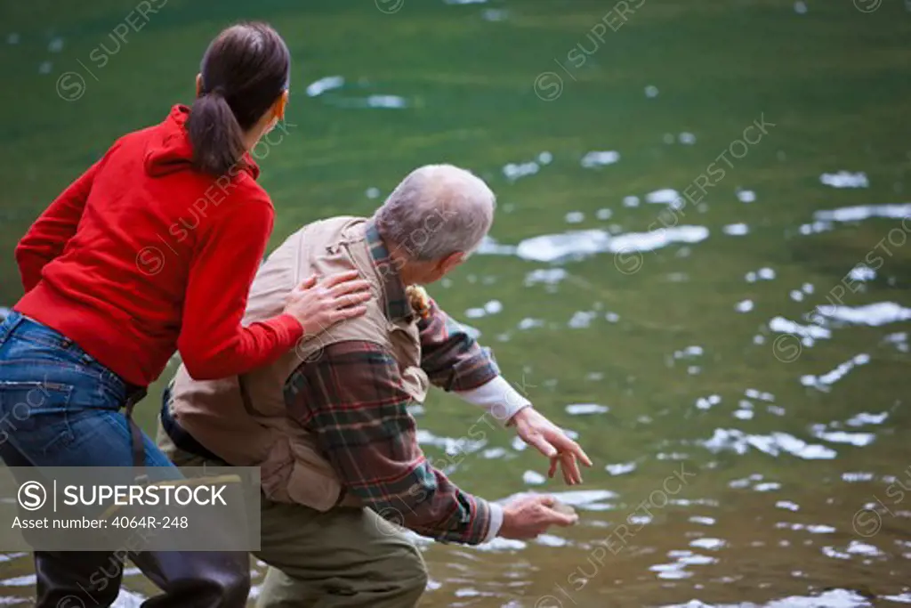 USA, Washington, Vancouver, Rear view of couple skipping stones on river