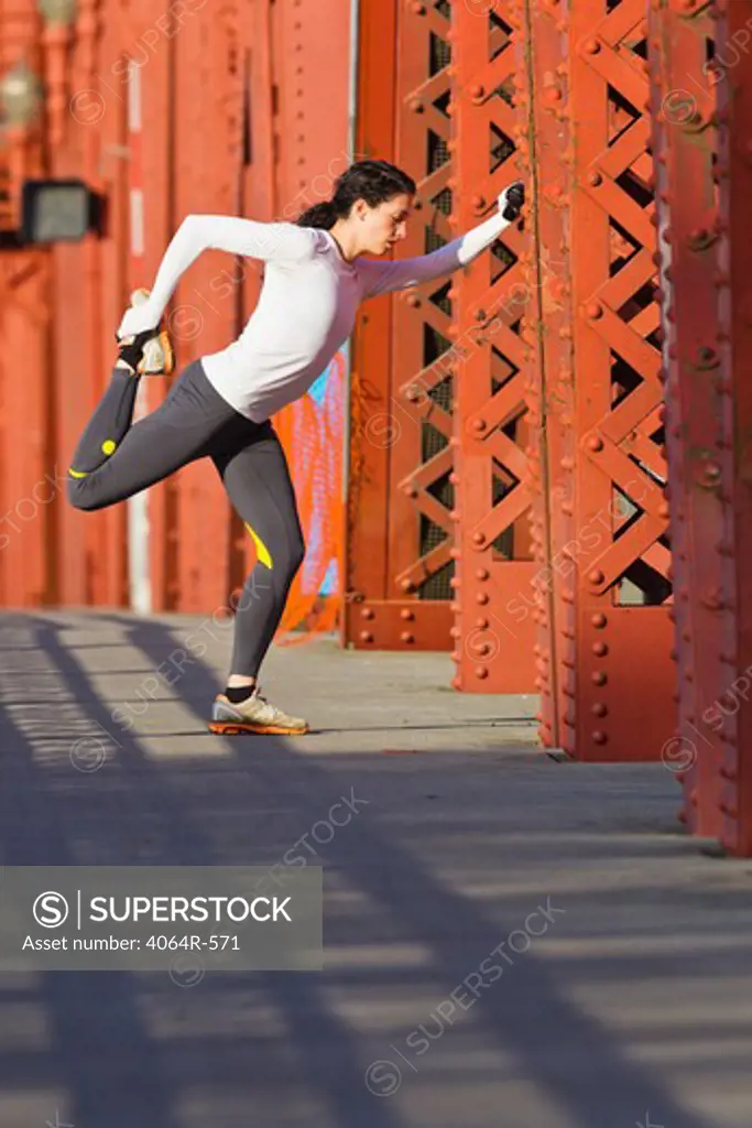 Female jogger, stretching on bridge