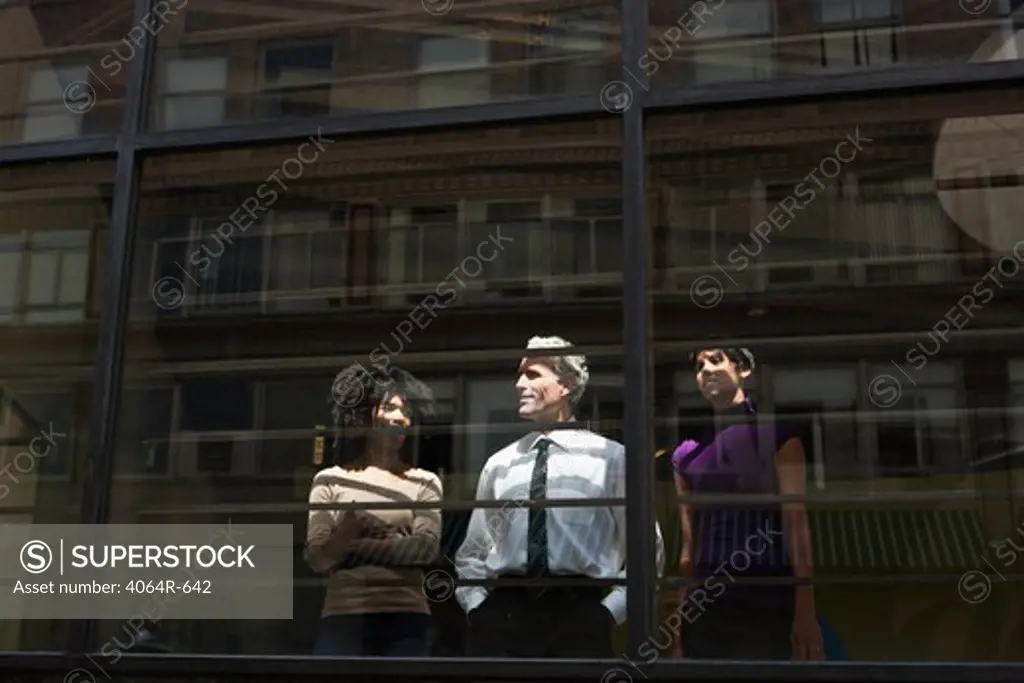 Two businesswomen looking through office window with businessman