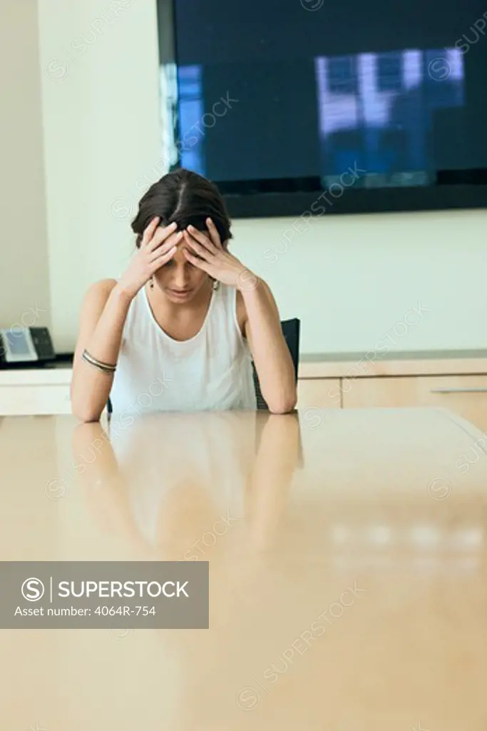 Woman sitting with head in hands at boardroom table