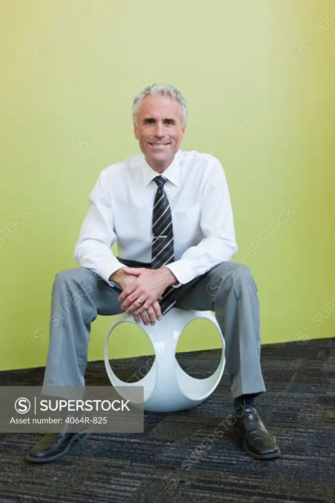 Portrait of mature businessman sitting on designer chair against yellow background