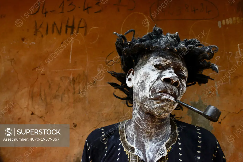 A man represents a sick and smoking character,  in a voodoo ceremony in the village of Bohicon, Benin. January 2020