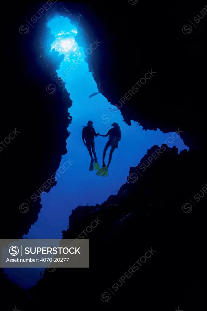 Two divers silhouetted at entrance of a coral cave, East End, Grand Cayman, Cayman Islands, British West Indies, Caribbean Sea. Model released