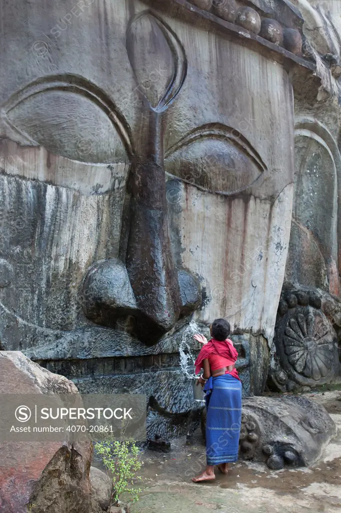 Pilgrim carrying out morning cleaning ritual on a carving of Shiva at 7th-9th century Hindu sacred site. Unakoti, Tripura, India, March 2012.
