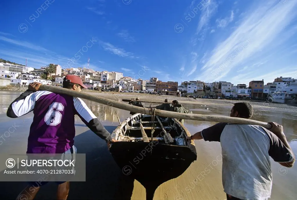 Men hauling fishing dory (boat) out of the water, Tagazout, Morocco.