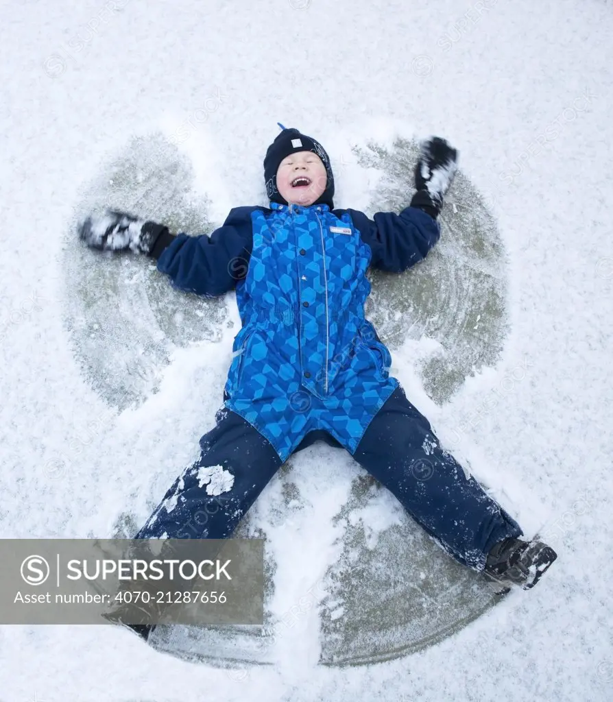 Child lying in the snow creating snow angel, Norway, January 2014. Model released.