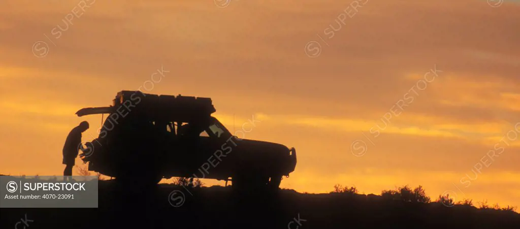 Man loading four-wheel drive vehicle at sunset in the Kalahari desert, Kgalagadi NP, South Africa