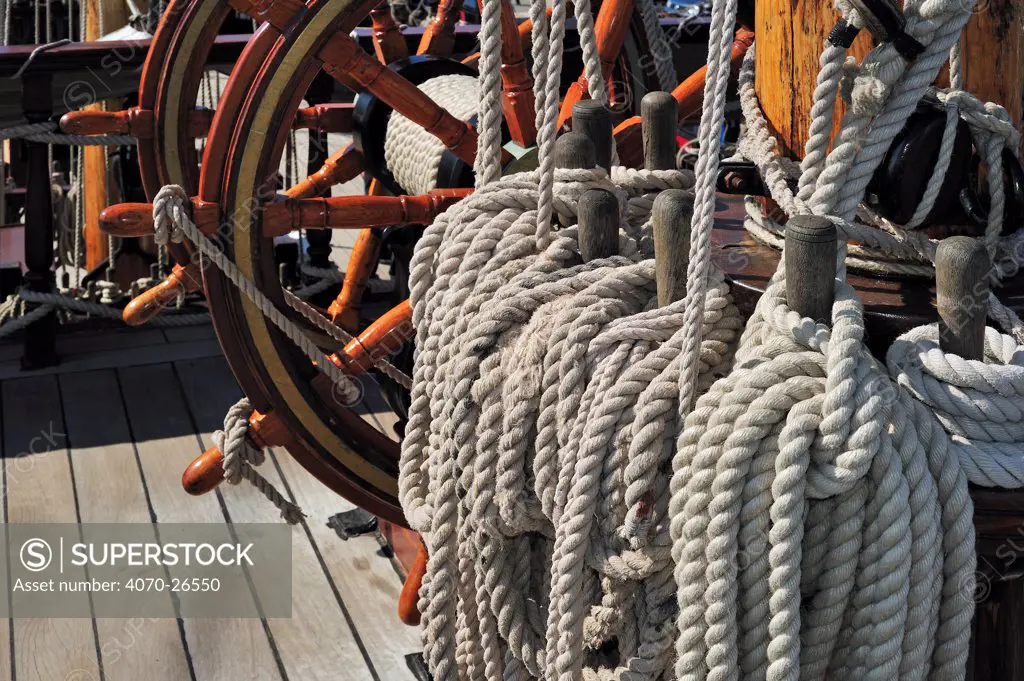 Steering wheel and ropes coiled around belaying pins aboard the 'Grand Turk / Etoile du Roy', a three-masted sixth-rate frigate built in 1996 as a replica of HMS Blandford, built in 1741, Saint Malo, Brittany, France, September 2010