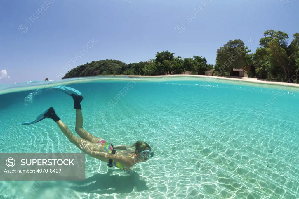 Split level shot of snorkler swimming in clear shallow water over sand, Malaysia.