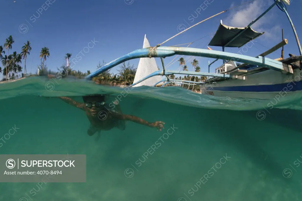 Split level view of diver under traditional outrigger banca fishing boat, Philippines