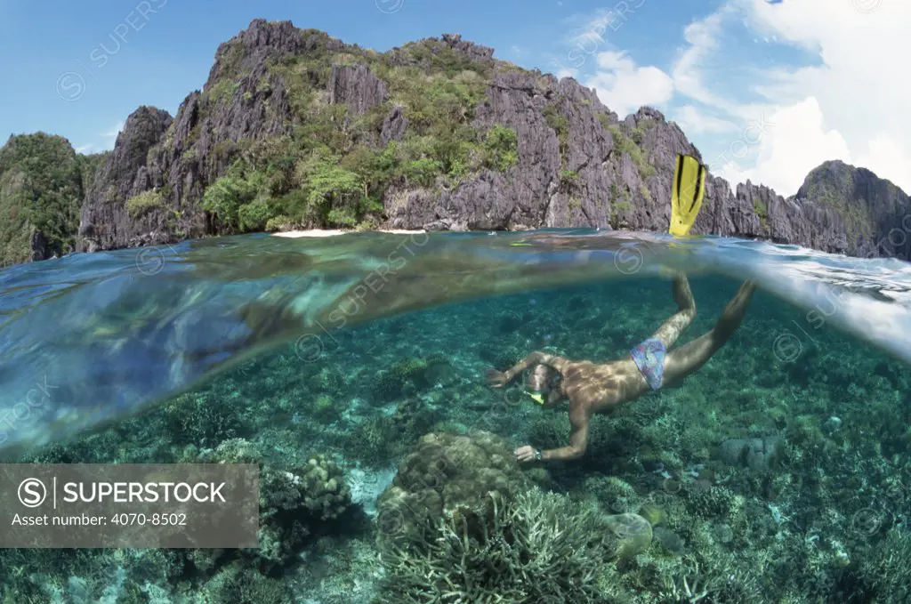 Split level of snorkler diving over coral reef near island, Palawan, Phillippines