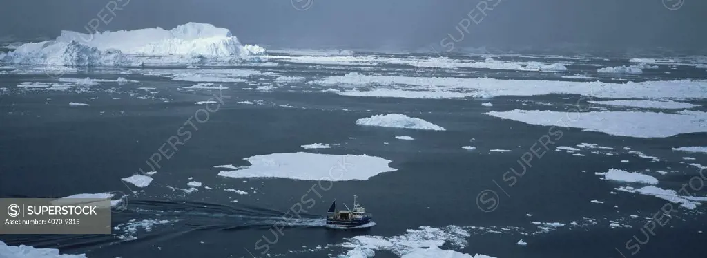 Fishing boat amongst Icebergs and melting ice in Disko Bay, Greenland